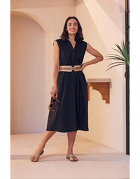Woman in a black dress with a belt standing in a bright room.