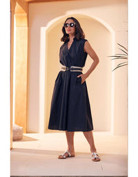 Woman in a navy dress with a belt standing in a sunlit archway.