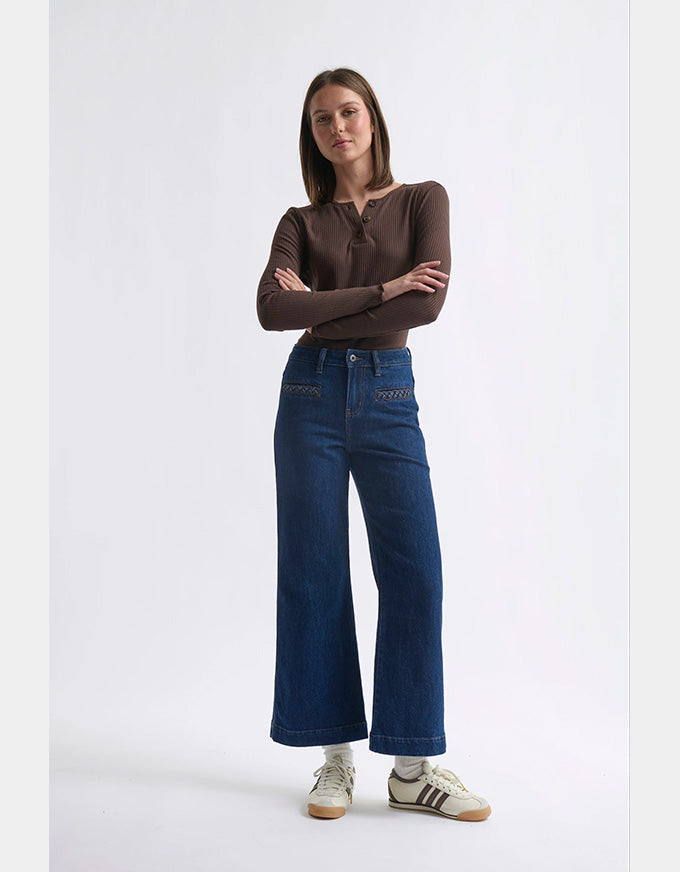 Woman wearing a brown long-sleeve top and blue jeans on a white background