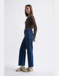 Woman wearing blue jeans and a brown top on a white background