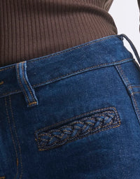 Close-up of blue jeans with braided detail on a white background