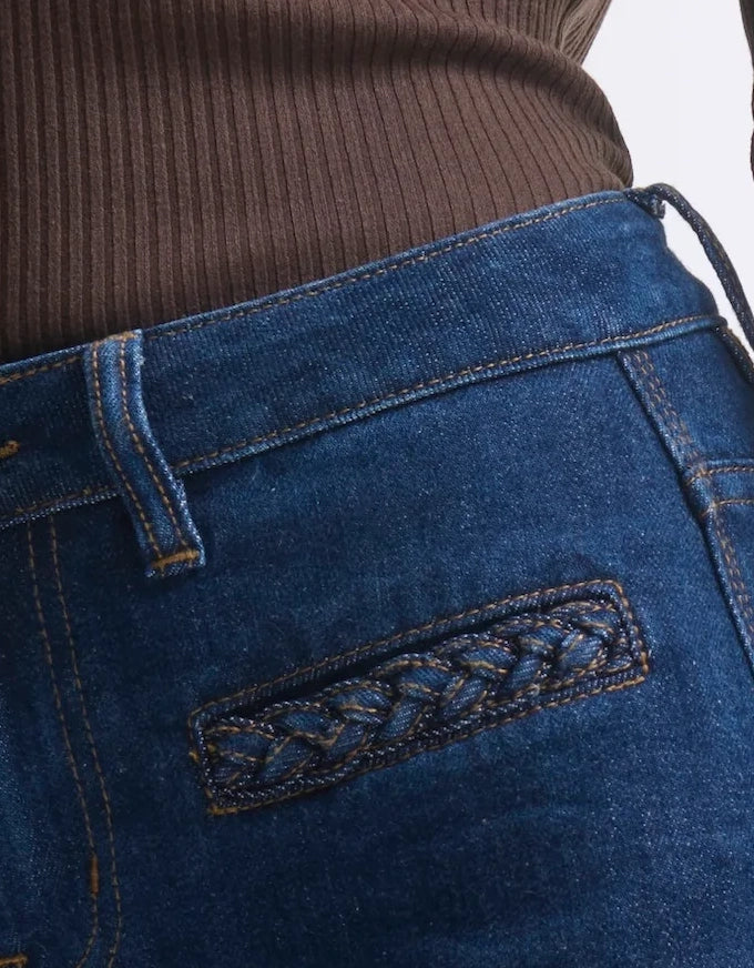 Close-up of blue jeans with braided detail on a white background