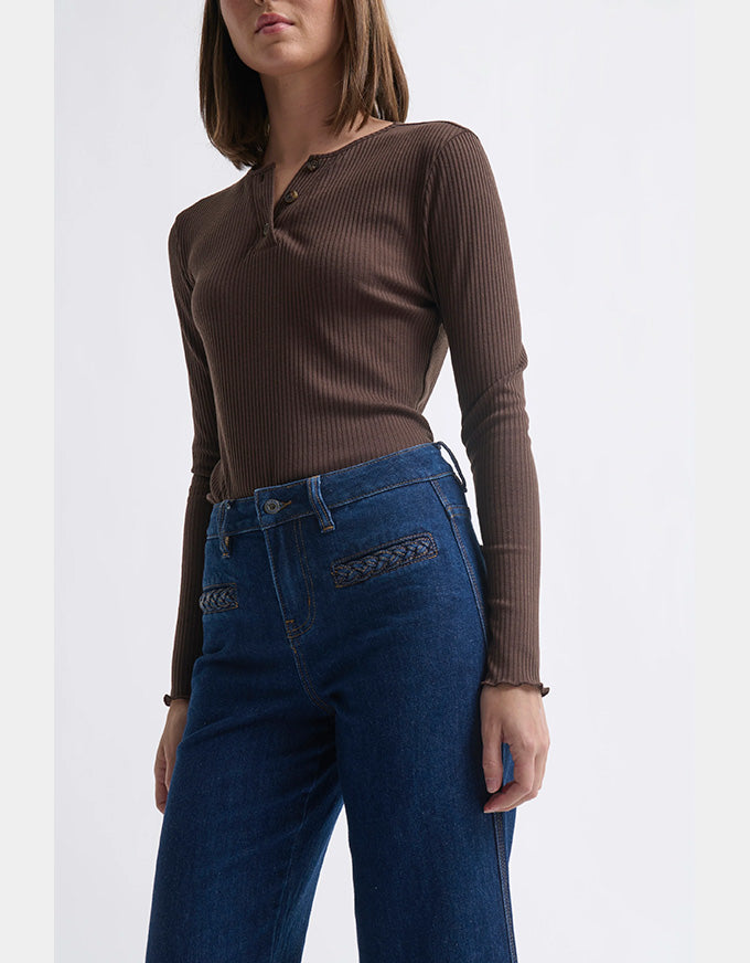 Woman wearing a brown ribbed long-sleeve top and blue jeans on a white background