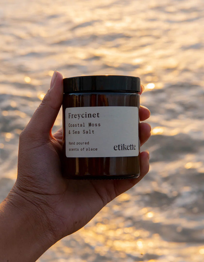 Hand holding a Freycinet product with a sunset over water background