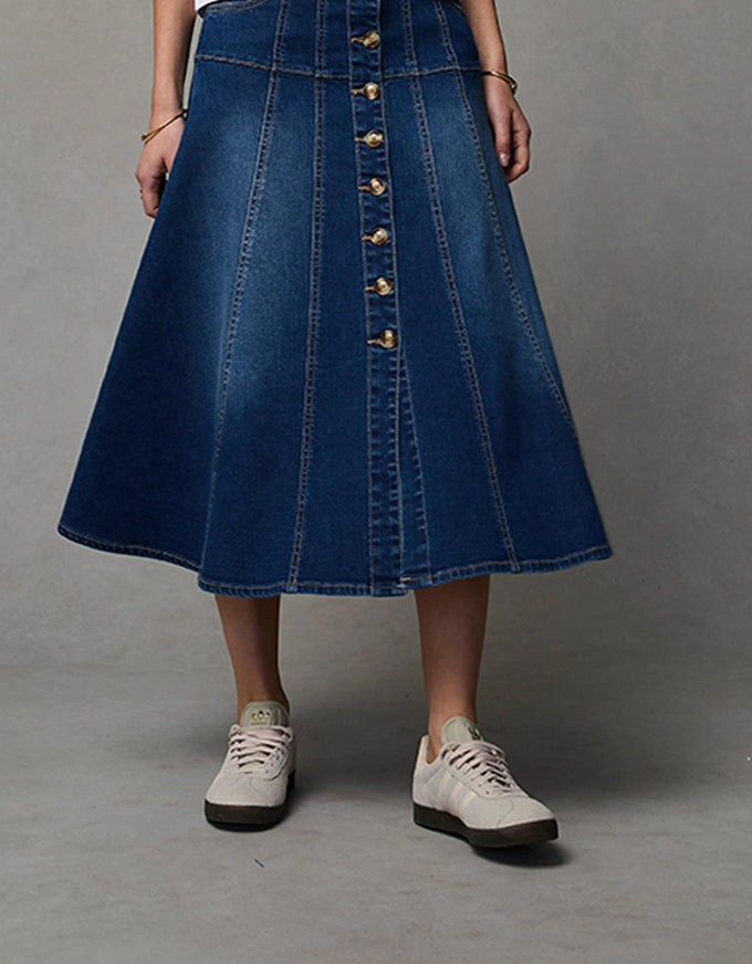 Person wearing a blue denim skirt with gold buttons on a gray background