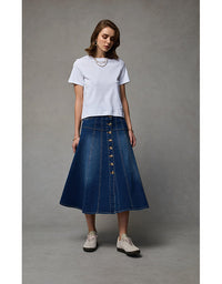 Woman wearing a white t-shirt and blue denim skirt against a gray background