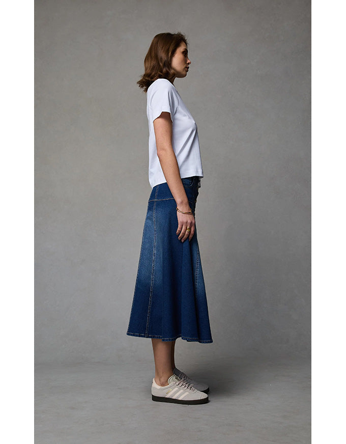 Woman wearing a white t-shirt and blue denim skirt on a gray background