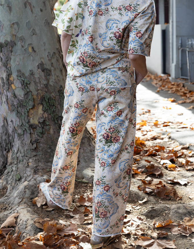 A person wearing a matching short-sleeve button-up shirt and wide-leg trousers set in an outdoor setting with a large tree trunk and scattered dry leaves on the ground.