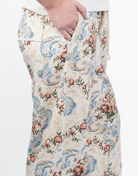 Close-up of a person wearing patterned trousers, showing a hand pulling the zipper and the fabric's ornate floral and scroll design in blue, beige, and brown tones.