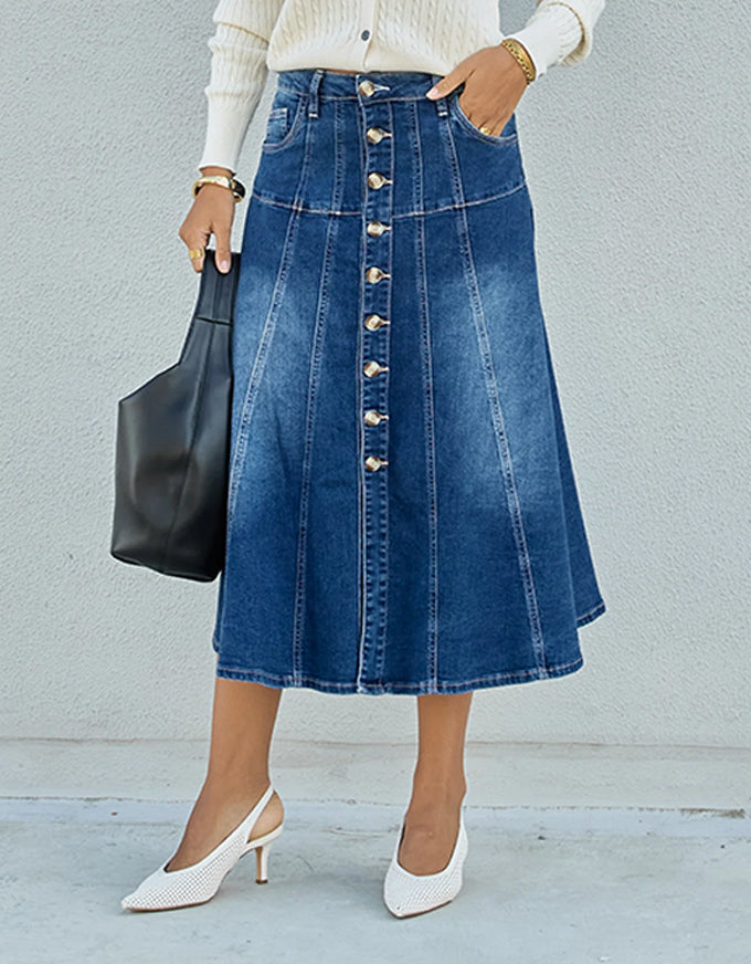 Person wearing a blue denim skirt with a button-down front, holding a black handbag against a light gray background.