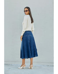 Woman wearing a white sweater and blue denim skirt against a light gray background