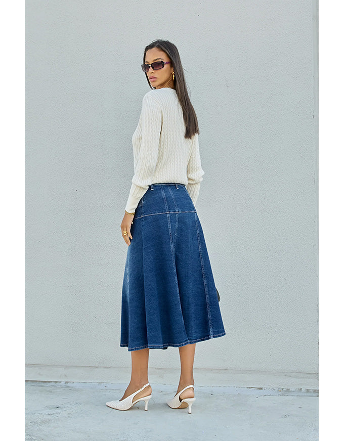Woman wearing a white sweater and blue denim skirt against a light gray background