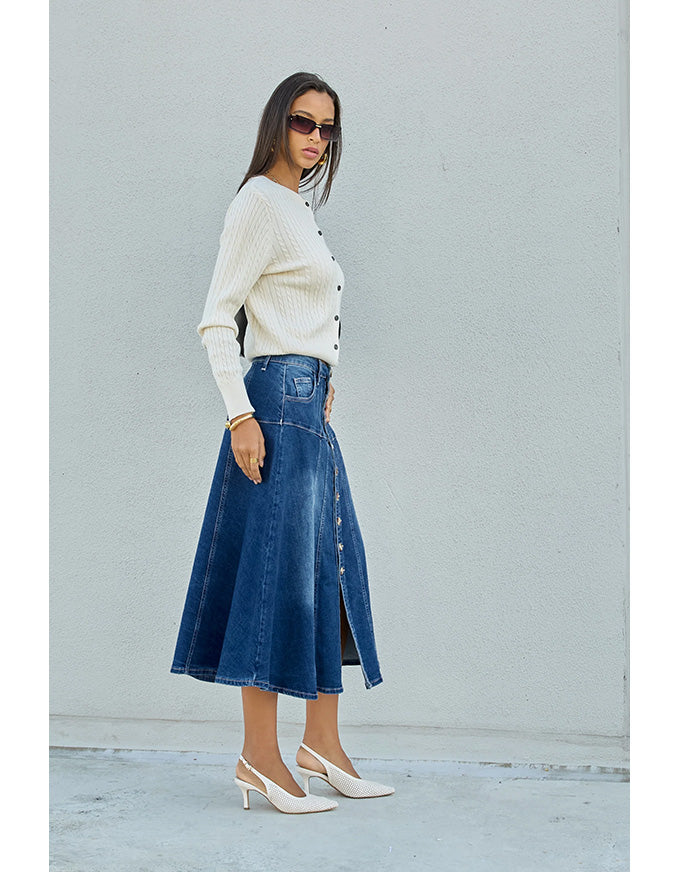 Woman wearing a white sweater and blue denim skirt against a gray background