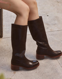 Brown knee-high boots worn by a person sitting on a stone bench.