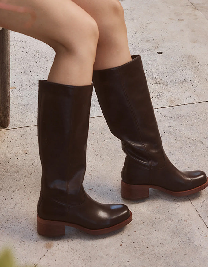 Brown knee-high boots worn by a person sitting on a stone bench.