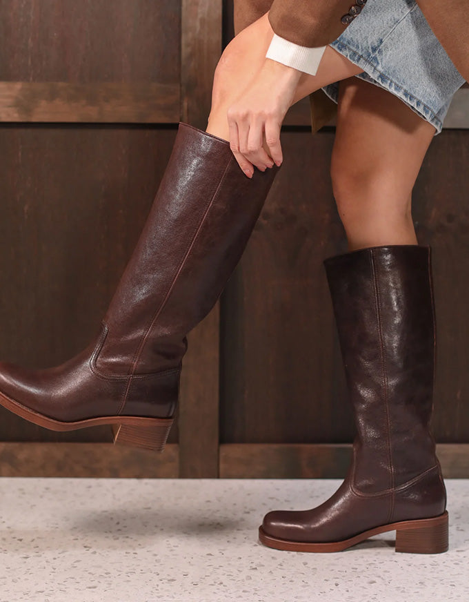 Brown leather knee-high boots worn by a person against a neutral background