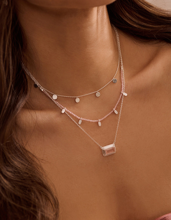 Close-up of a woman wearing multiple necklaces with a neutral background