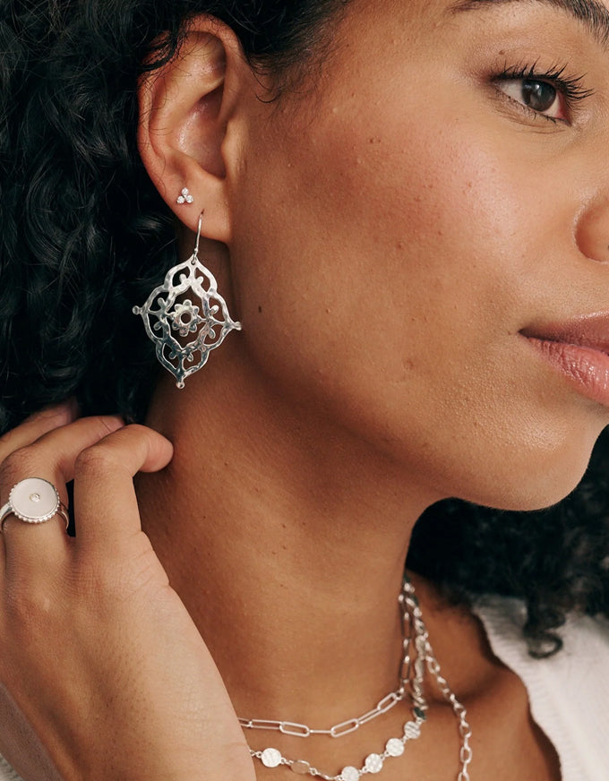 Close-up of a woman wearing silver earrings and a ring, with a blurred background.