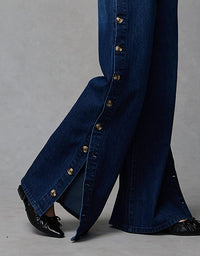 Close-up of a person wearing blue jeans with gold buttons on a gray background