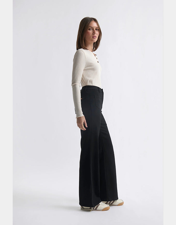 Woman wearing a white long-sleeve top and black wide-leg pants on a light gray background