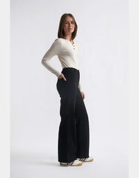 Woman wearing a white long-sleeve top and black wide-leg pants on a light gray background