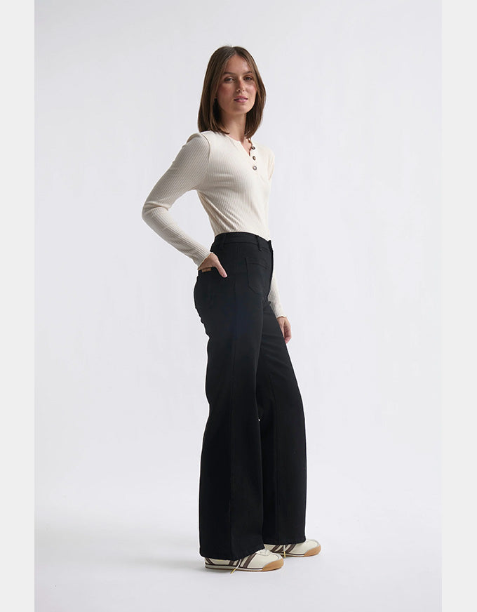 Woman wearing a white long-sleeve top and black wide-leg pants on a light gray background