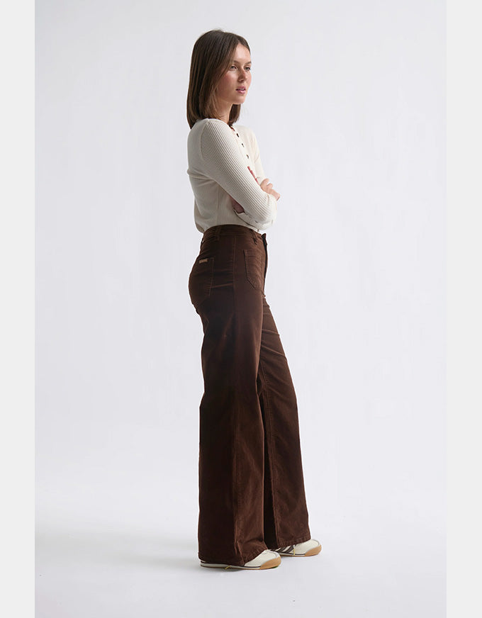 Woman wearing brown wide-leg pants and a white top on a light gray background