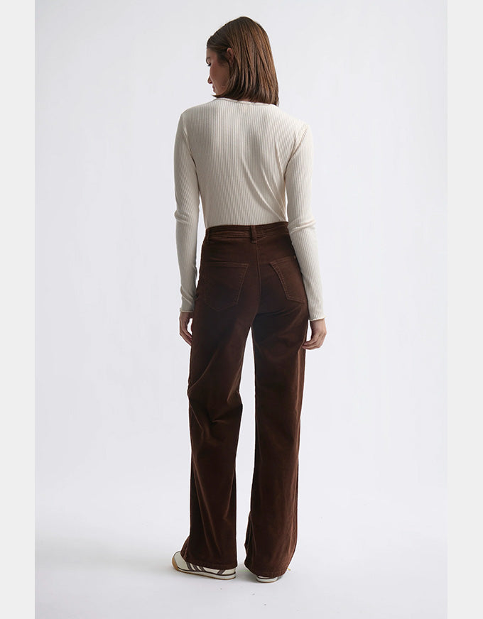Person wearing a white long-sleeve top and brown pants on a white background