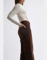 Person wearing a white long-sleeve top and brown wide-leg pants on a light gray background
