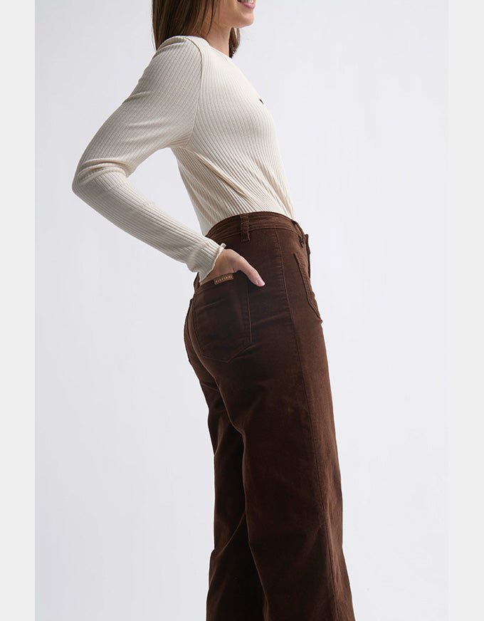 Person wearing a white long-sleeve top and brown wide-leg pants on a light gray background