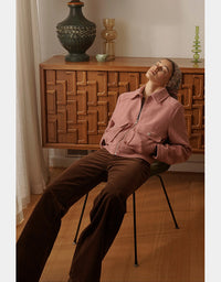 Person sitting on a chair wearing a pink jacket and brown pants in a room with wooden furniture and decor.