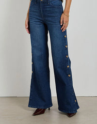 Blue jeans with button details worn by a person on a plain background