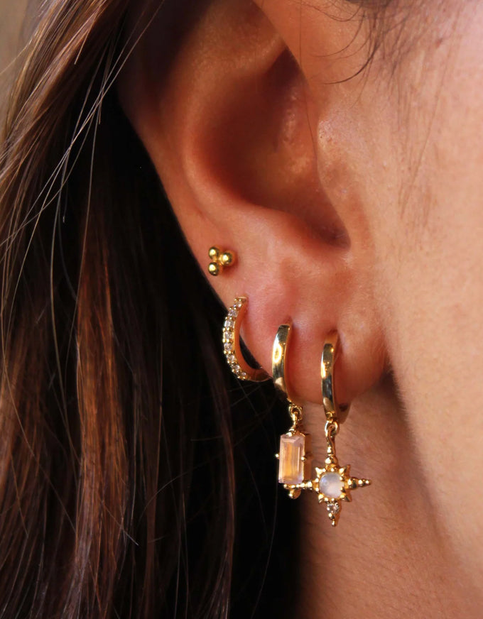 Close-up of an ear wearing gold hoop earrings with a star design.