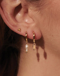 Close-up of an ear wearing gold hoop earrings with a pearl accent.