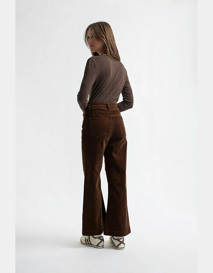 Woman wearing brown flared pants and a matching top on a white background