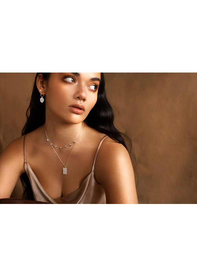 Woman wearing a necklace and earrings against a brown background