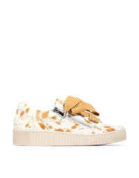 Sneaker with cow print pattern and tan bow on a white background