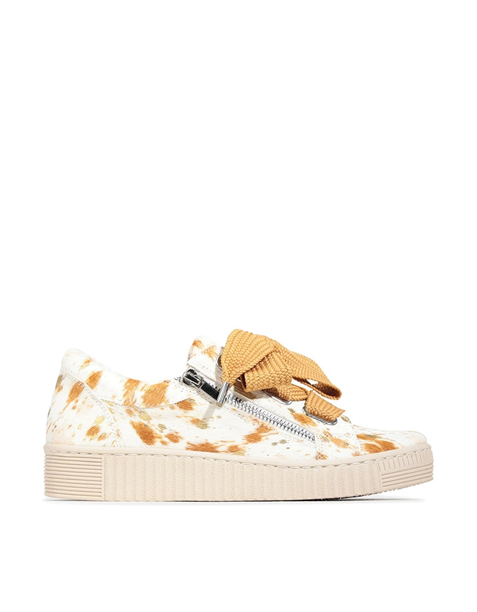Sneaker with cow print pattern and tan bow on a white background