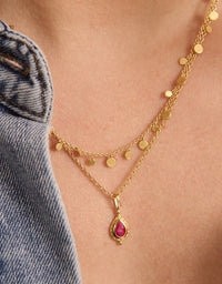 Gold necklace with a red gemstone pendant on a person wearing denim jeans.