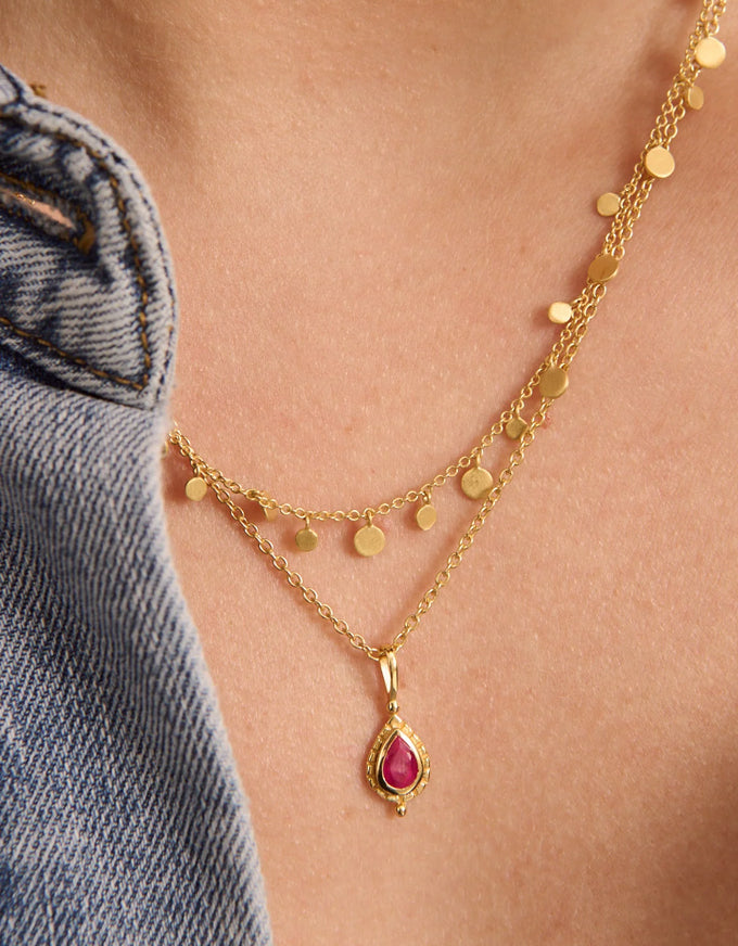 Gold necklace with a red gemstone pendant on a person wearing denim jeans.