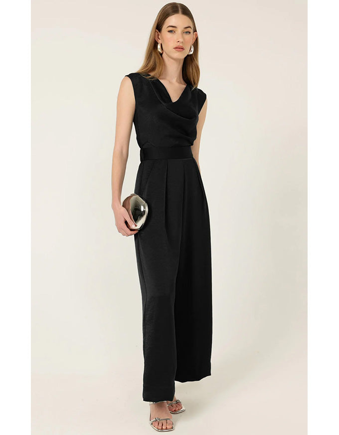 Woman wearing a black jumpsuit holding a clutch against a white background