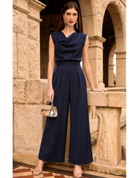 A woman models a navy blue sleeveless wide-leg jumpsuit with a draped cowl neckline, standing in front of a stone archway.