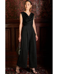 Woman wearing a black jumpsuit in an elegant room with wooden paneling.