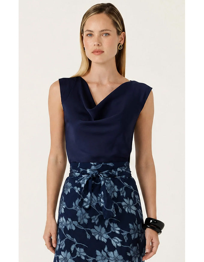 A woman modeling a sleeveless navy top with a draped neckline and a matching navy floral skirt with a tie waist, against a plain light background.