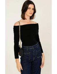 Woman wearing a black off-shoulder top and blue jeans with a small black handbag.