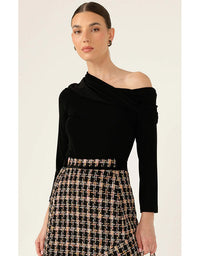 Woman wearing a black off-shoulder top and plaid skirt on a beige background