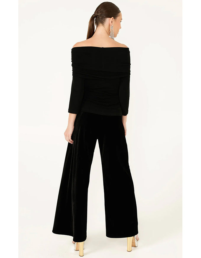 Woman wearing a black off-shoulder top and wide-leg pants on a white background