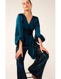 Woman wearing a teal top and black sequin pants against a white background