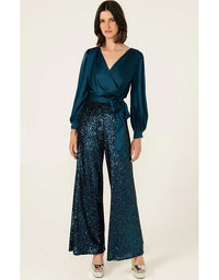 Woman wearing a teal wrap top and sequin pants on a white background