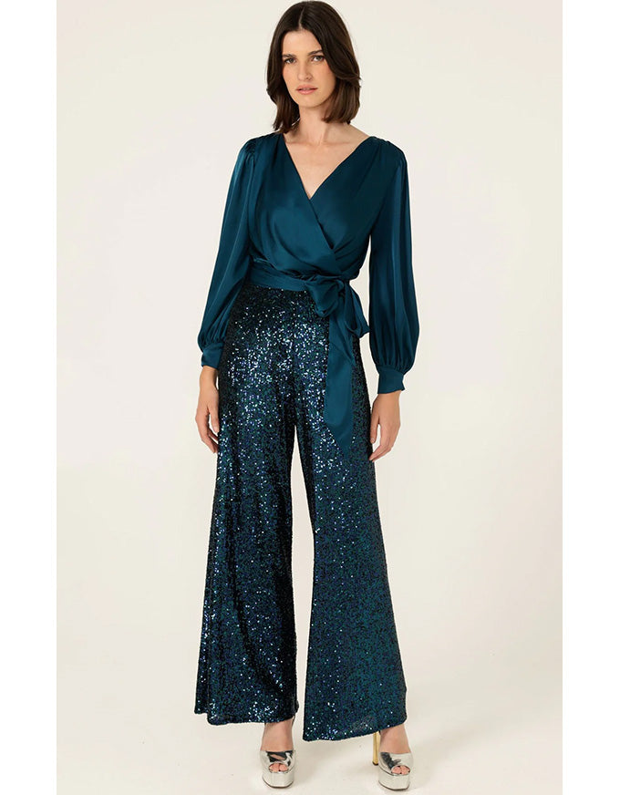 Woman wearing a teal wrap top and sequin pants on a white background